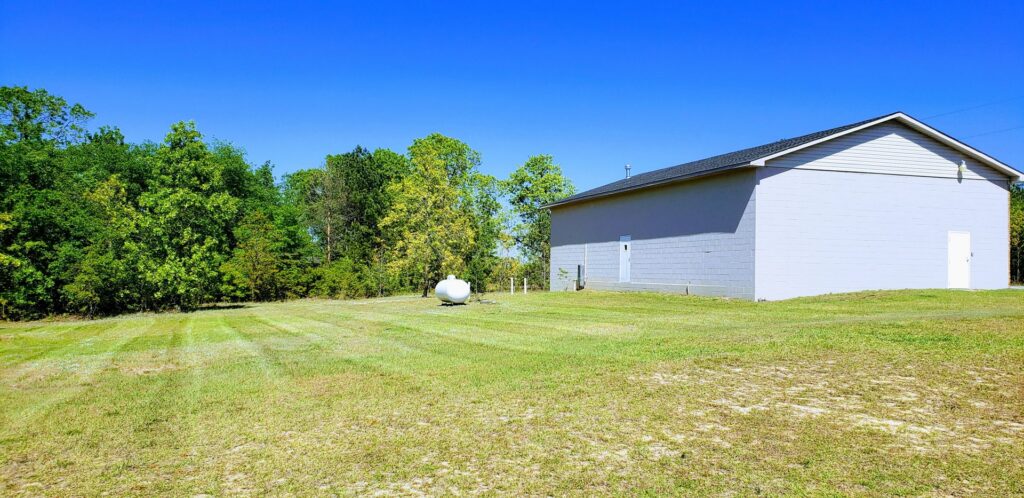A large, freshly mowed field next to a commercial building, showcasing extensive lawn care by Liberty LAWN Care in Sumter, SC.