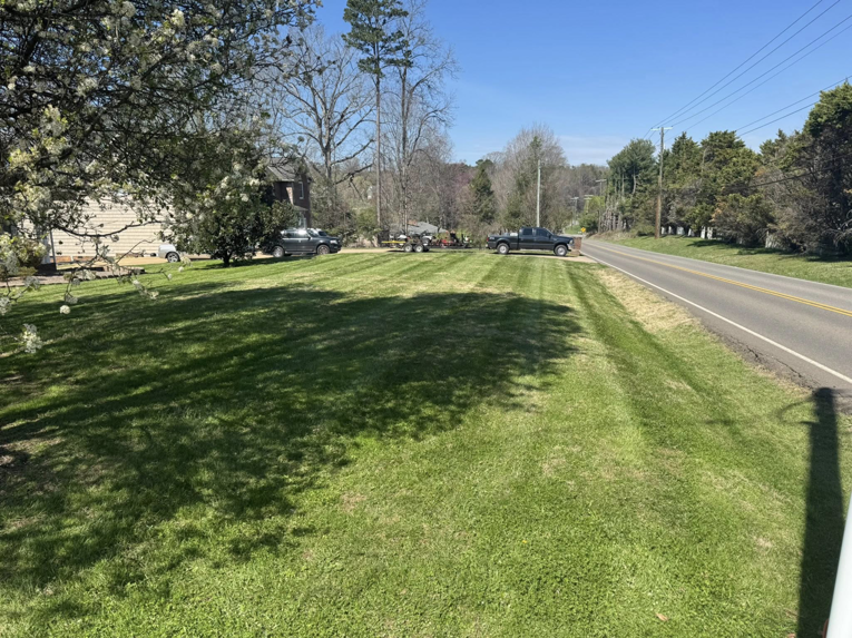 A large, freshly mowed lawn alongside a road, with a lawn care truck and trailer in the background from Hancock Lawn Care in Knoxville, TN.