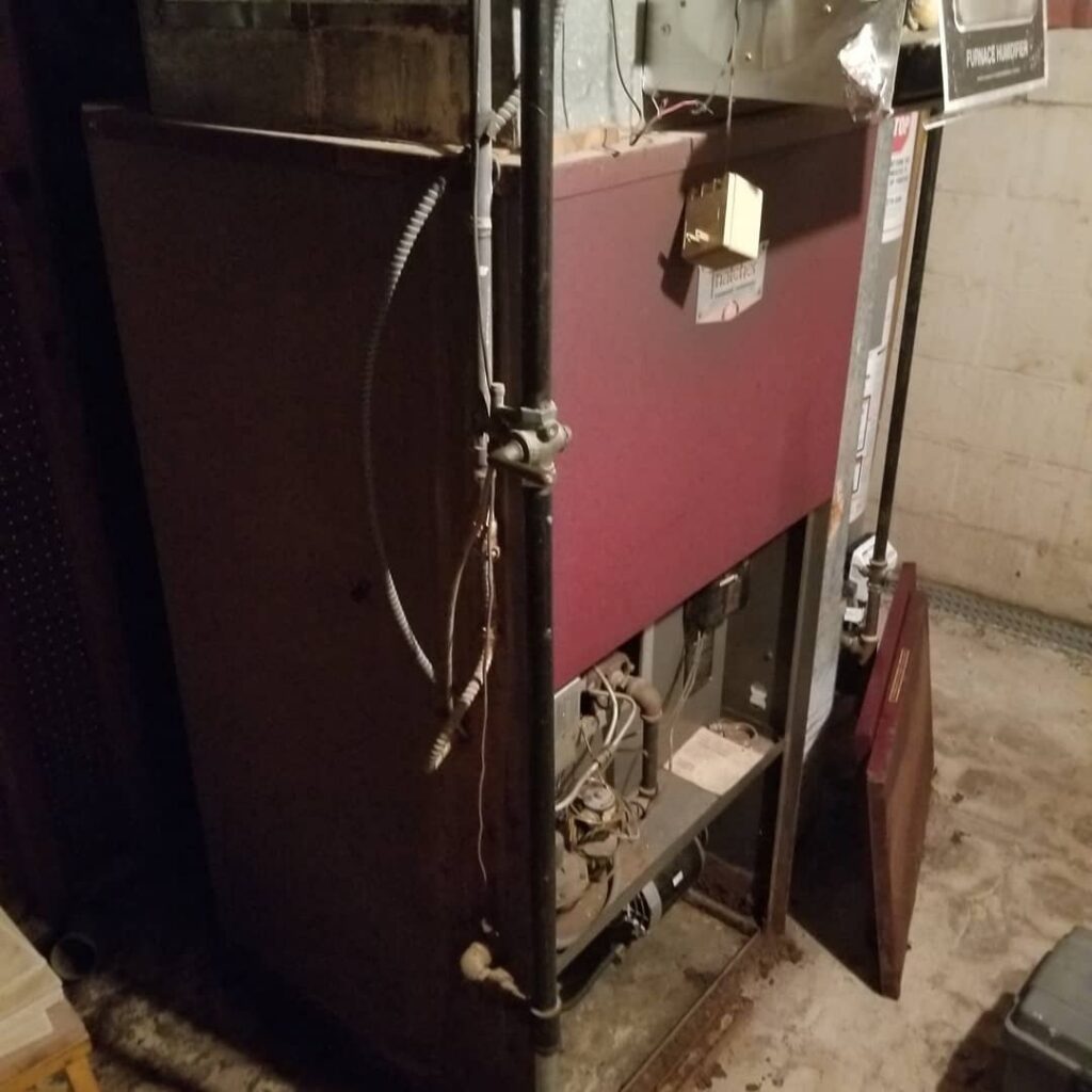 A large, older furnace or boiler unit in a basement, indicating a heating system service by Batista Heating & Cooling, LLC in Charlotte, NC.