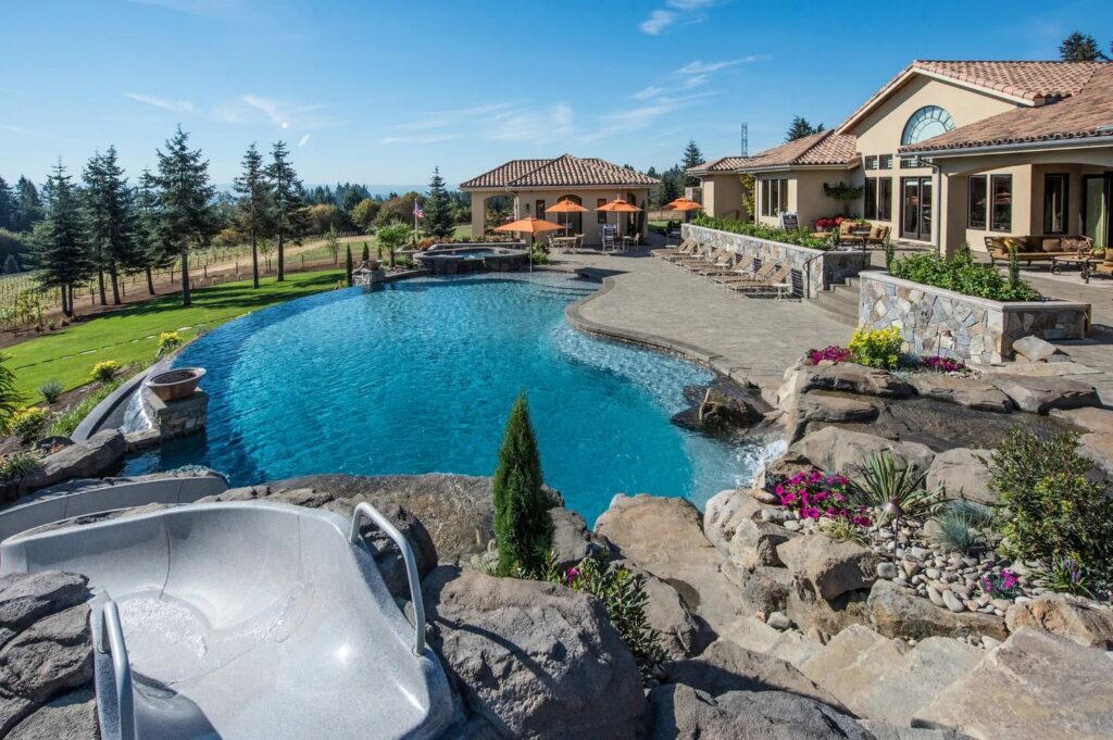 A large custom outdoor pool area with a spa, slide, and rock features, designed by Anderson Poolworks in Wilsonville, OR.