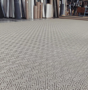 Large patterned carpet laid out in a showroom with many carpet rolls in the background at Odino Designs, llc in Portland, OR.