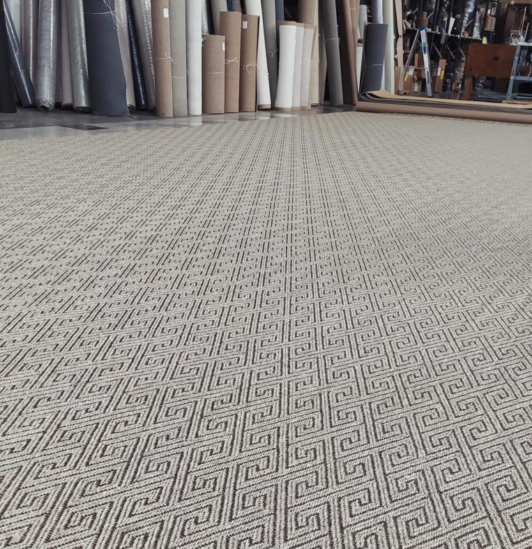 Large patterned carpet laid out in a showroom with many carpet rolls in the background at Odino Designs, llc in Portland, OR.
