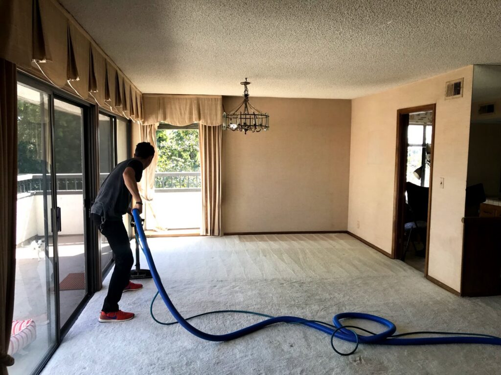 A professional cleaning a large carpeted room with a cleaning wand and hose for Mark it Clean Carpet & Upholstery Cleaning Long Beach, CA.