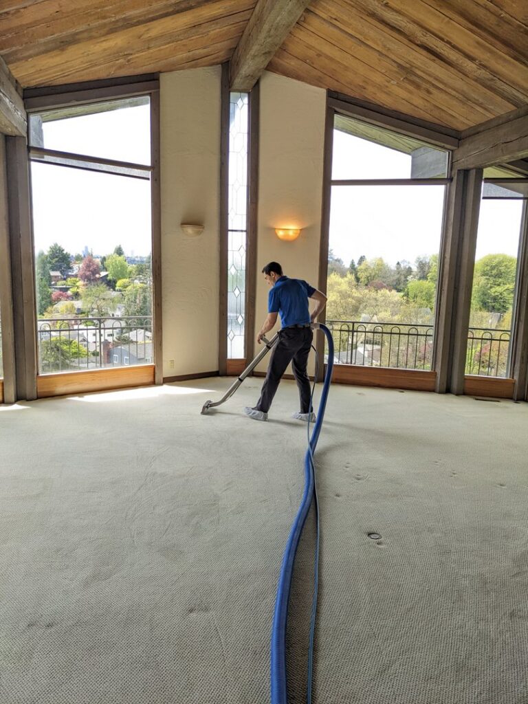 A technician from North Seattle Carpet Cleaning cleaning a large, light-colored carpet in a spacious room in Seattle, WA