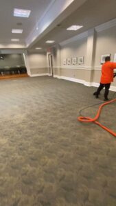 A professional cleaning a large carpeted room with a carpet cleaning wand by Treo General Services of North Carolina LLC in Durham, NC.