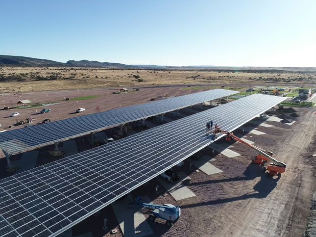 An aerial view of a large-scale solar panel installation project with workers on the panels by Pueblo Electrics, Inc. in Pueblo, CO.