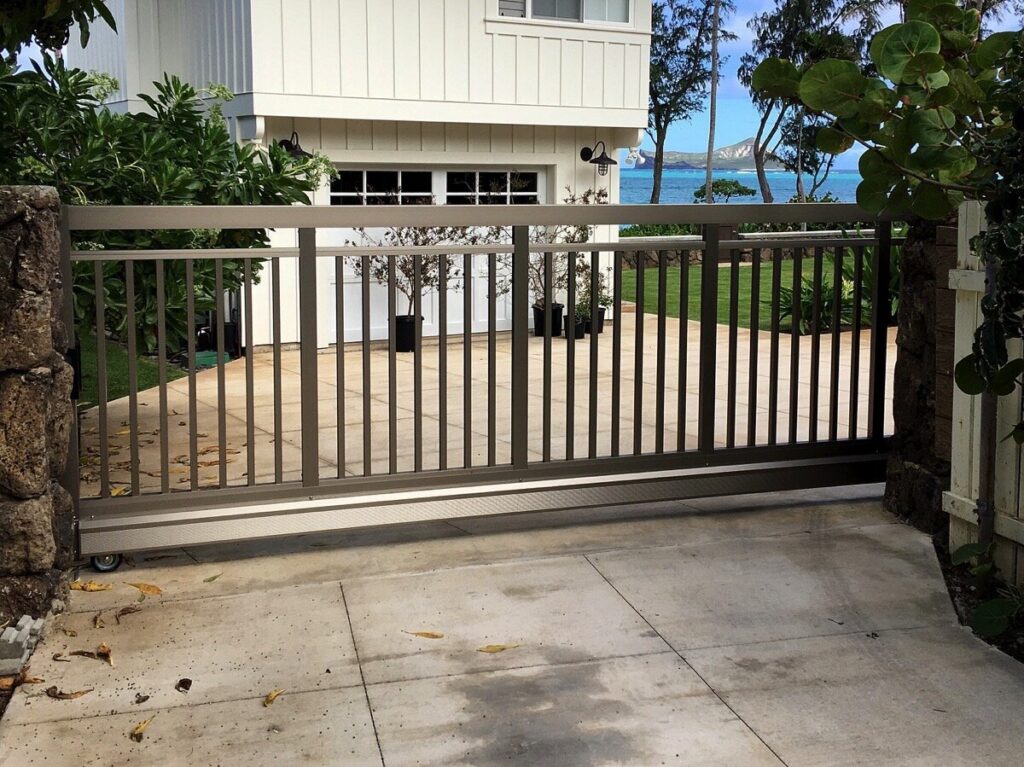 A large sliding gate with vertical slats installed at a driveway entrance by KunkelWorks Hawaii in Mililani, HI.