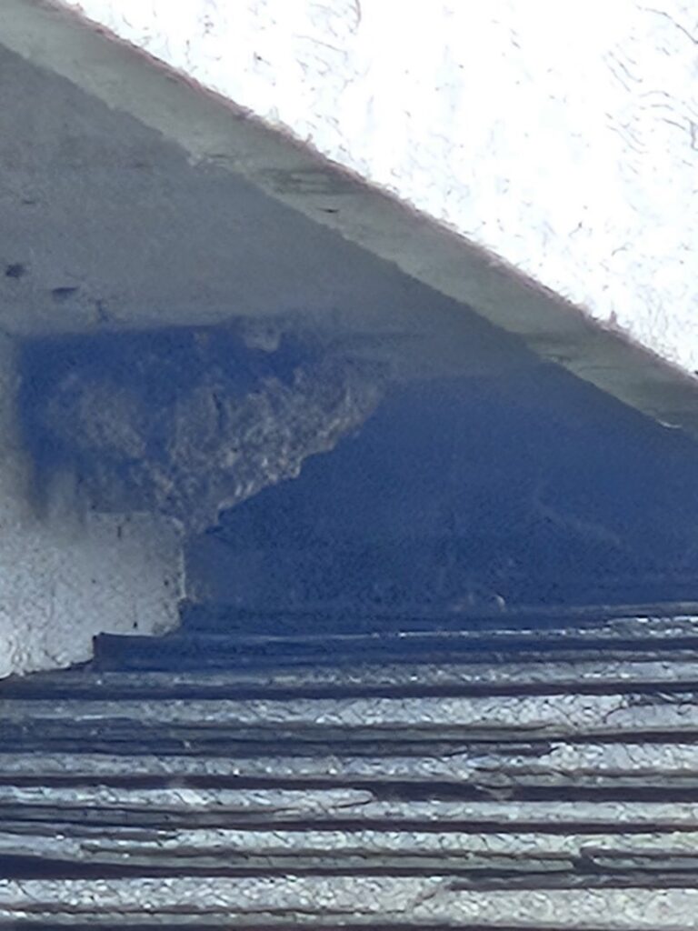 A large wasp or hornet nest visible under the eaves of a roof, indicating a pest removal job by Comprehensive Pest Solutions in Toledo, OH.