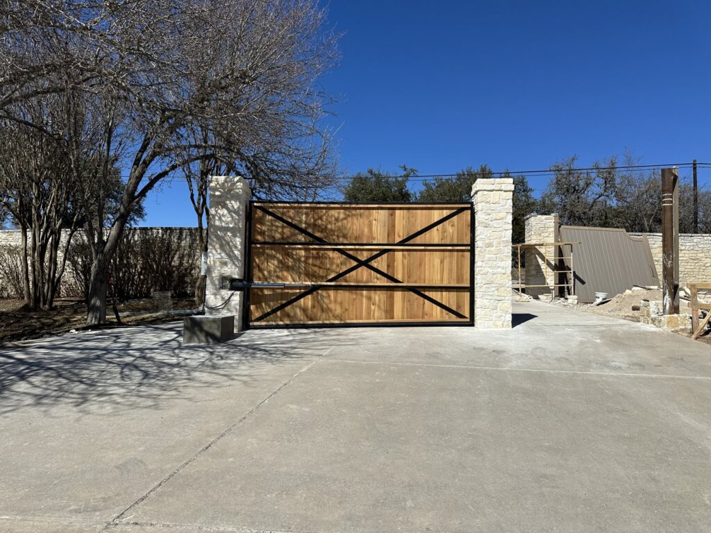 A large wooden automatic gate with elegant stone pillars, installed by Stand Strong Fencing of East Austin, TX.