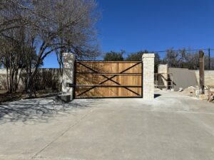 A large wooden automatic gate with elegant stone pillars, installed by Stand Strong Fencing of East Austin, TX.