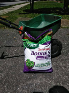 Lawn care products including a bag of weed and feed next to a spreader, used by DLC Service in Kenner, LA.