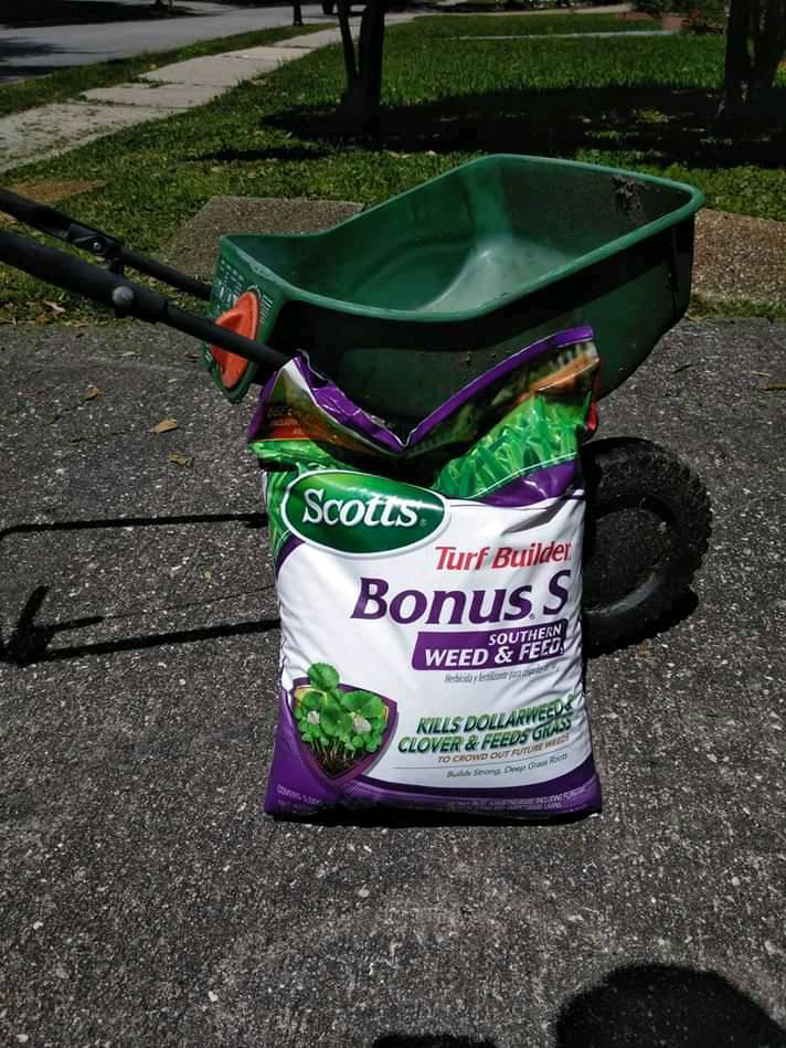 Lawn care products including a bag of weed and feed next to a spreader, used by DLC Service in Kenner, LA.