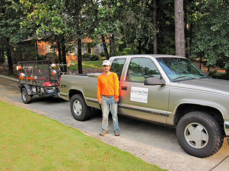 A lawn care professional with a branded truck and equipment trailer from Guy Next Door Lawn Care, LLC in Birmingham, AL.