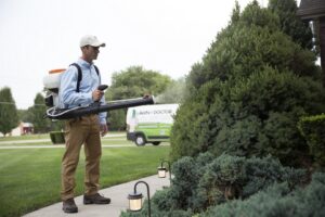 A Lawn Doctor specialist spraying shrubs with a backpack sprayer in Carmel, IN, providing tree and shrub care.