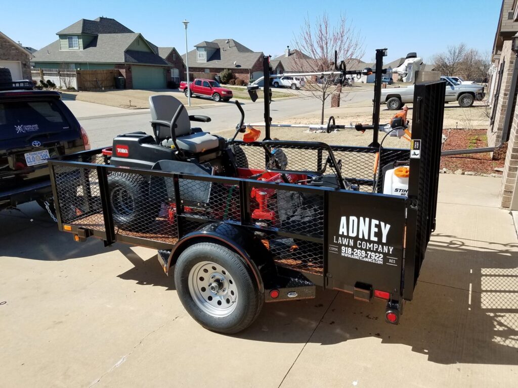 A professional lawn care trailer loaded with a riding mower and trimmers, ready for service by A&B Lawn Services in Baytown, TX.