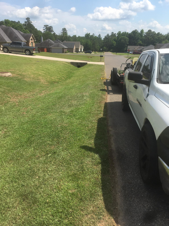 A white pickup truck with a trailer carrying lawn care equipment parked on the street by a well-maintained lawn by Taylor Cutts lawn Care Service llc in Shreveport, LA