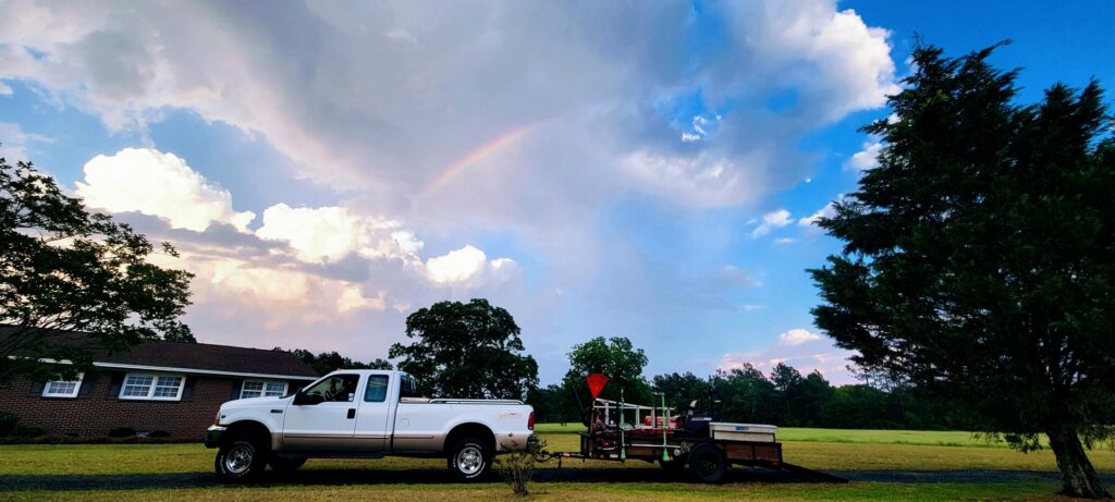 A Liberty LAWN Care truck and equipment trailer parked under a beautiful rainbow in Sumter, SC, ready for service.