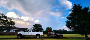 A Liberty LAWN Care truck and equipment trailer parked under a beautiful rainbow in Sumter, SC, ready for service.