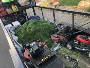 A trailer loaded with professional lawn mowers and fresh grass clippings, ready for disposal by Front Range Finest in Fort Collins, CO.