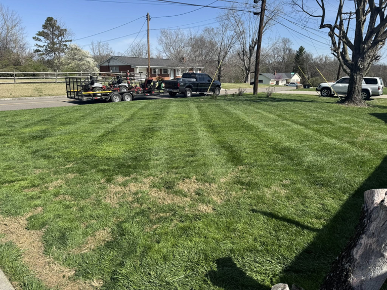 A truck and trailer with professional lawn mowing equipment parked on a freshly striped lawn by Hancock Lawn Care in Knoxville, TN.
