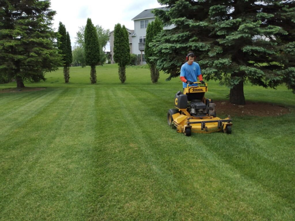 A Three Boys Lawncare professional operating a zero-turn mower, providing expert lawn mowing service in Rochester, MN.