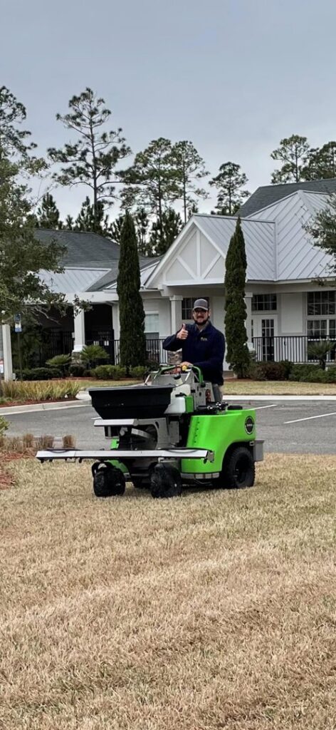 A Pro Care Lawn and Pest technician using a ride-on spreader for lawn pest control in Jacksonville, FL.