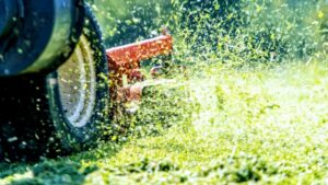 A close-up of a lawnmower actively cutting grass, with clippings flying, by Grassology Lawn Care in Montgomery, AL