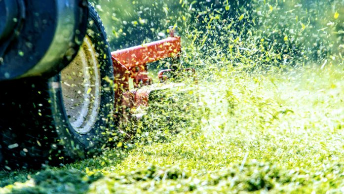 A close-up of a lawnmower actively cutting grass, with clippings flying, by Grassology Lawn Care in Montgomery, AL