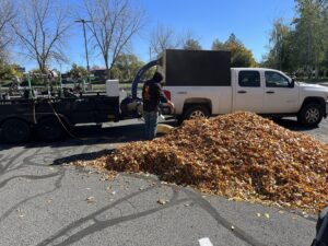 A lawn care crew member using a large leaf vacuum to clear a massive pile of autumn leaves, a service by McLain Lawn & Landscape in Spokane, WA.