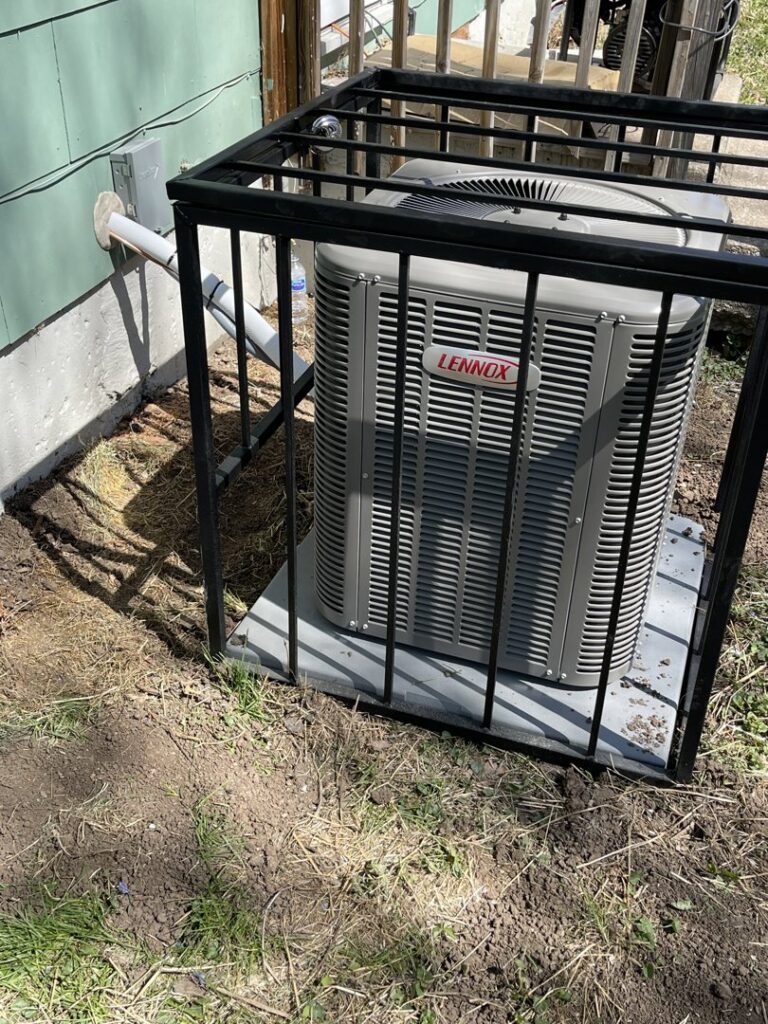 A Lennox outdoor AC unit protected by a metal cage, installed by Spartan Mechanical KC in Spring Hill, KS.