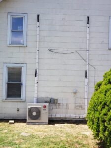 An LG mini-split condenser unit with line sets running up the exterior wall of a house, installed by Tack Mechanical LLC in Baltimore, MD.