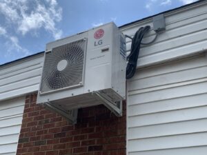 An LG Smart Inverter mini-split outdoor unit installed on a brick wall by Trinity Climate Control in Clayton, NC.