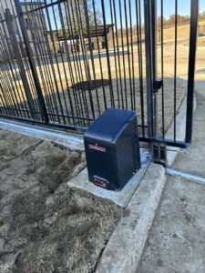 A LiftMaster automatic gate motor installed next to a black metal gate by Craftsman Automatic Gates in Dallas, TX.
