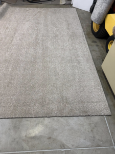 A light beige carpet piece laid on a concrete floor, ready for or after binding by Rug Edge Binding Company in Spokane, WA