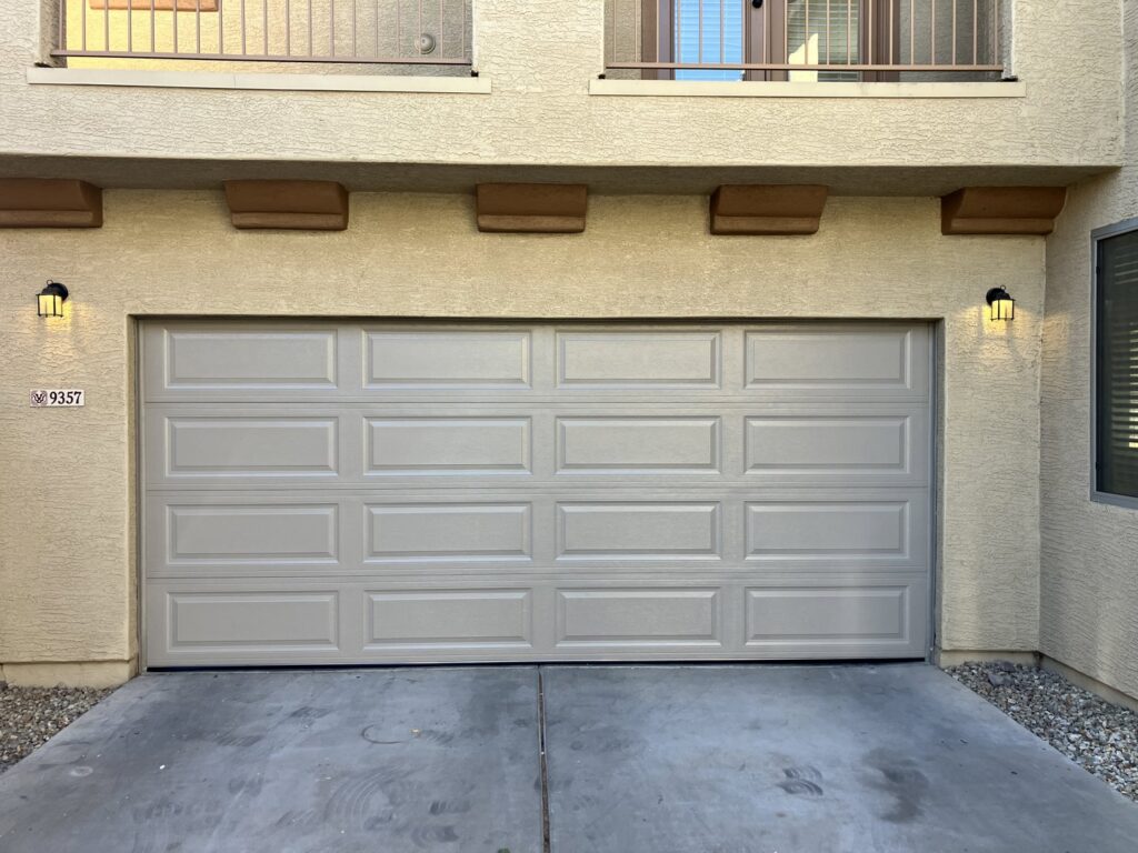 A newly installed light beige paneled garage door on a stucco house by Anew Garage by Jon's Garages in Surprise, AZ.