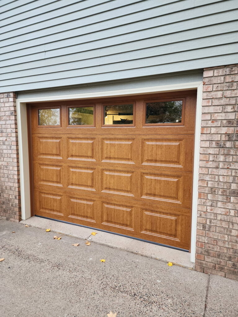 A light brown paneled garage door with windows installed on a brick house by LabraDoor Overhead Services in Eau Claire, WI.