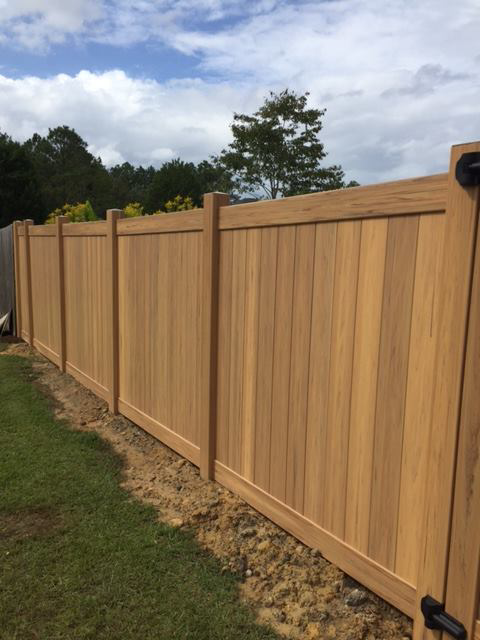 A newly installed light brown wood-look privacy fence extending along a property line by Custom Fence Builders in Gulfport, MS.