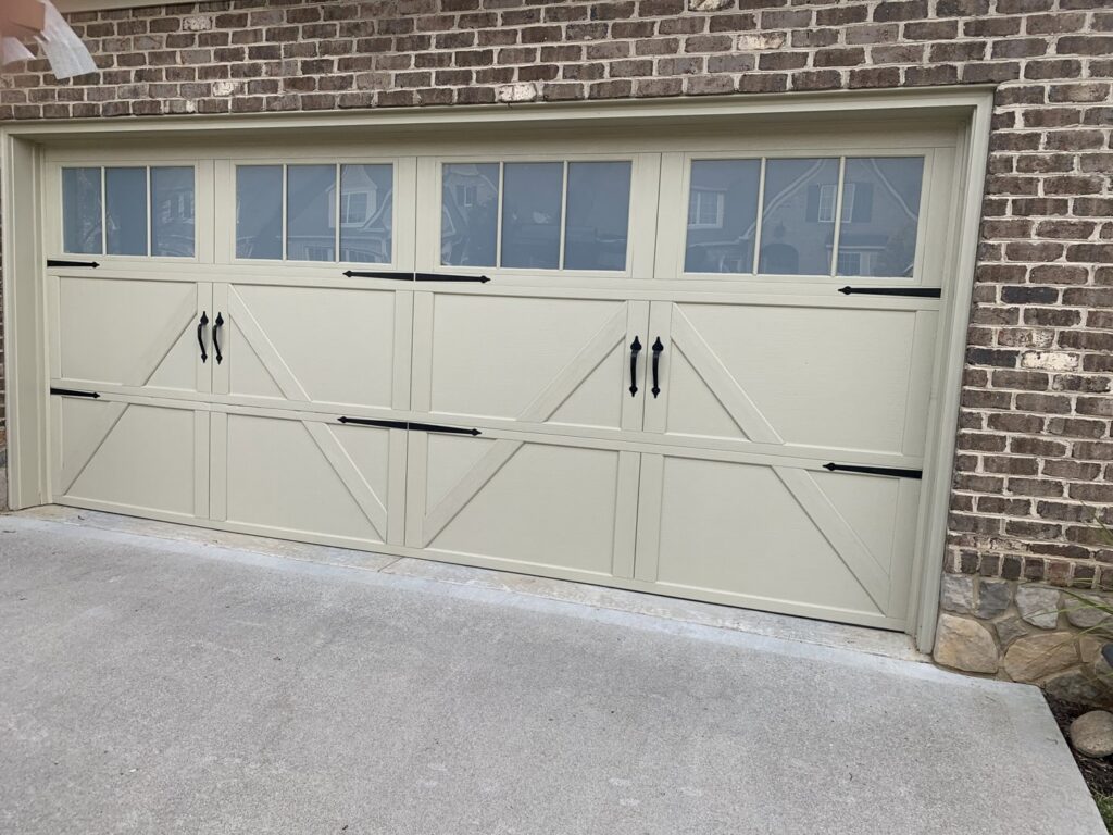 A light-colored garage door featuring decorative windows and hardware, installed on a brick home by Knox Garage Door Service LLC in Knoxville, TN.