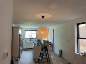 An electrician installing a new light fixture with a ladder in a room by Moss Contracting in Philadelphia, PA.