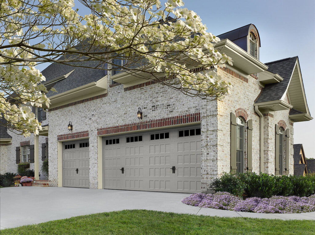Two light gray garage doors installed on a white brick house by Access Garage Doors-Chattanooga, TN