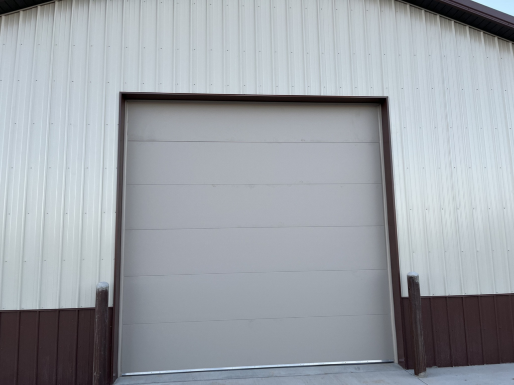 A light grey commercial garage door on a two-tone building by Usa Garage Door Services and Construction, LLC at 1206 E 6th St, USA.