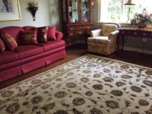 A light-colored oriental rug beautifully placed in a living room with a red sofa and an armchair by Brandon Oriental Rugs in Furlong, PA.