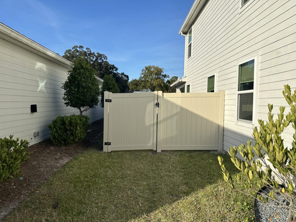 A light-colored privacy fence with a double gate installed in a residential backyard by Best Fence and Rail in Jacksonville, FL.