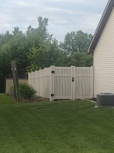 A light-colored vinyl privacy fence with a gate installed next to a house by Nailed It Fencing and Exteriors in Evansville, IN.