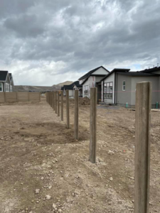 A long line of concrete fence posts installed, with a completed fence section in the distance by BroKrete Fencing LLC in Salt Lake City, UT
