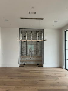 A linear chandelier installed in a dining room with a modern wine cellar by Focal Electric Company in Dallas, TX.