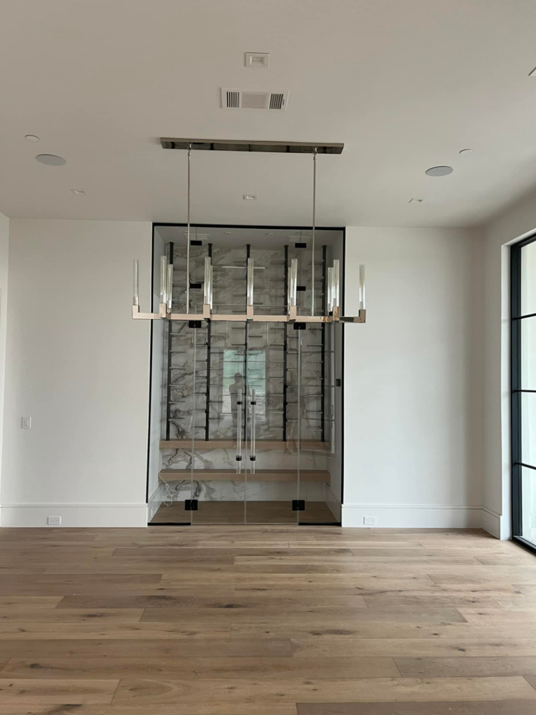 A linear chandelier installed in a dining room with a modern wine cellar by Focal Electric Company in Dallas, TX.
