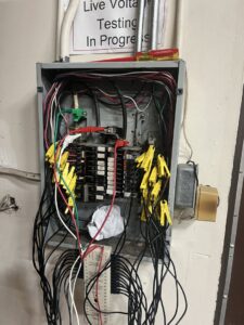 An open electrical panel with wires and testing clips, showing live voltage testing by Mountain Electric in Knoxville, TN.