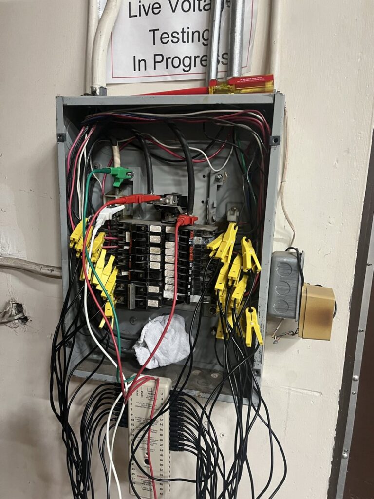 An open electrical panel with wires and testing clips, showing live voltage testing by Mountain Electric in Knoxville, TN.