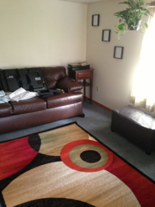 A modern area rug with circular patterns placed over existing carpet in a living room by Sunshine Rugs and Art in Londonderry, NH.